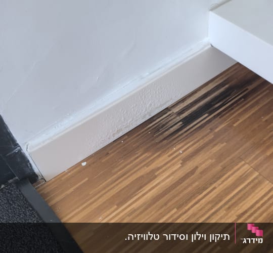 נזקי רטיבות וקילופי צבע בקיר ובפנל לצד רצפת פרקט